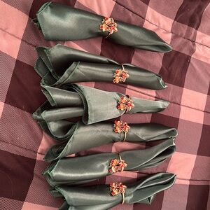 Six Christmas green napkins & six napkin rings that are holly berries & bells.